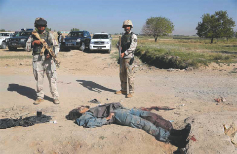 Afghan security forces stand guard at the body of an alleged Taleban insurgent in military uniform in Ghazni yesterday. Taleban insurgents in military uniform set off a car bomb and stormed an Afghan prison yesterday freeing hundreds of inmates and killi