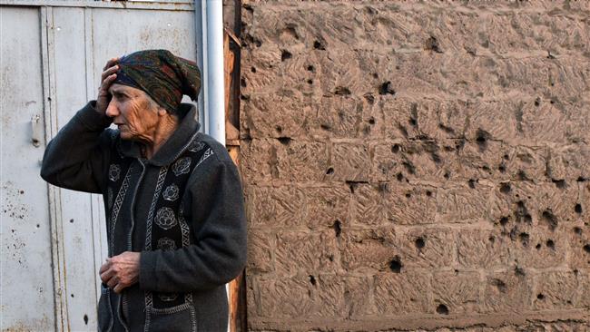 An elderly woman stands next to a wall damaged by shelling in the Armenian village of Movses close to the border with Azerbaijan