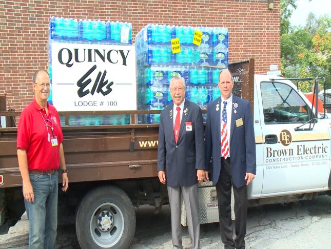 Three men stand in front of the water donated to the veterans home