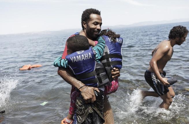 A migrant carries his two children as he gets off of an inflatable boat after arriving on the Greek island of Lesbos after crossing the Aegean sea from Turkey to Greece