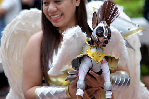 A participant carries a dog dressed as a warrior angel during a Halloween party for pets and kids at Eastwood Mall