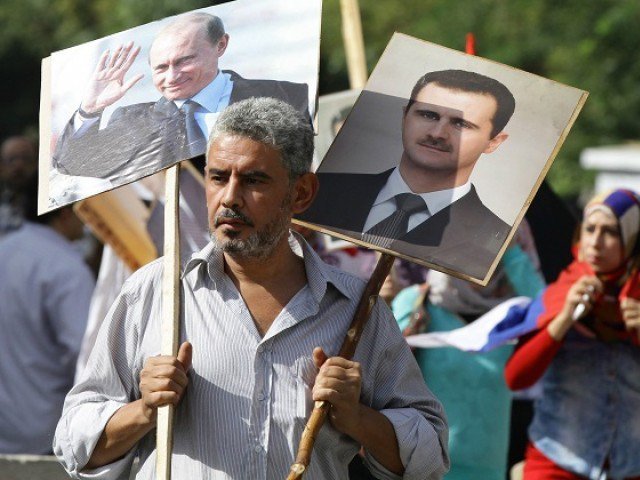 A Syrian man holding up portraits of President Bashar al Assad and his Russian counterpart Valdimir Putin joins several hundred people who gathered near the Russian embassy in Damascus