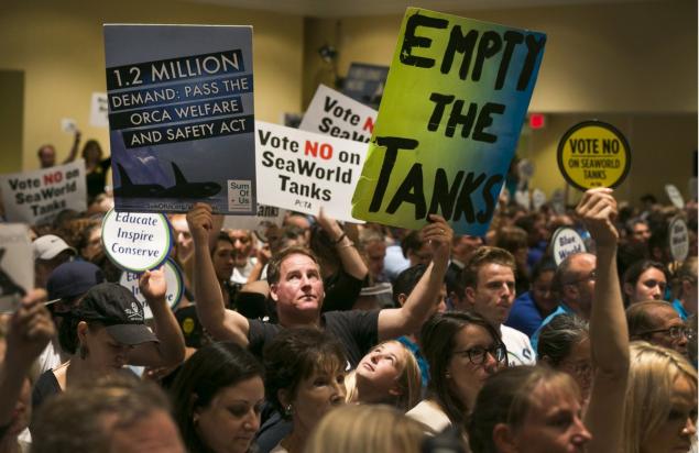 Animal rights activist Kirby Kotler with his daughter Kirra 12 from Malibu Calif. holds up signs as opponents and supporters fill the room during a California Coastal Commission meeting on Thursday in Long Beach Calif. The commission approved an exp