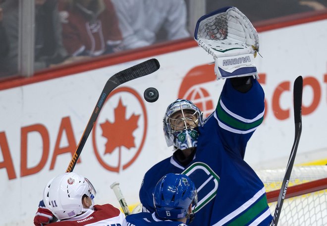 Vancouver Canucks goalie Ryan Miller right reaches for the puck with his glove as Montreal Canadiens Brendan Gallagher left tries to get his stick on it while Canucks Yannick Weber of Switzerland looks on during the second period of an NHL hockey