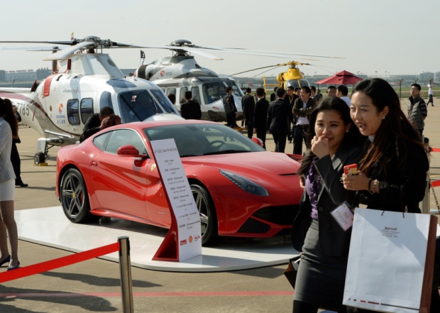 People walk past a Ferrari and helicopters at a conference in Shanghai