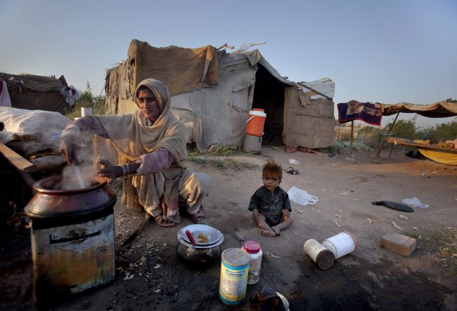 A Pakistani woman prepares food as her child plays on the ground outside their shanty on International Day for Eradication of Poverty at a slum in Islamabad Pakistan on Monday Oct. 17 2011. Pakistan is facing high poverty rate with a majority of peopl