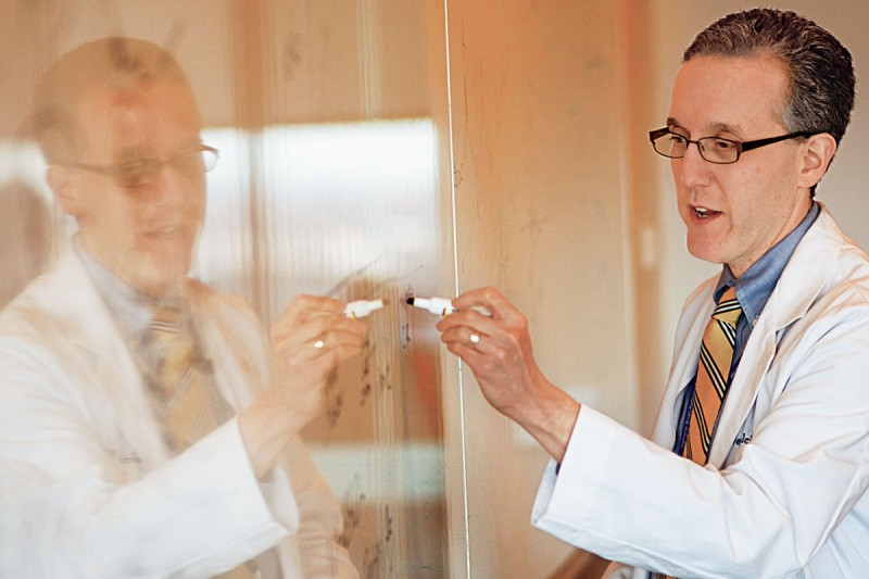 A doctor wearing a white lab coat writes on a white board with a marker