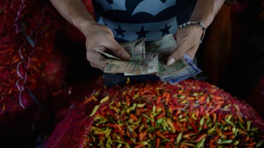 A vendor counts Indonesian rupiah banknotes near chili peppers sitting at a stall at the Pasar Induk Kramat Jati market in Jakarta Indonesia