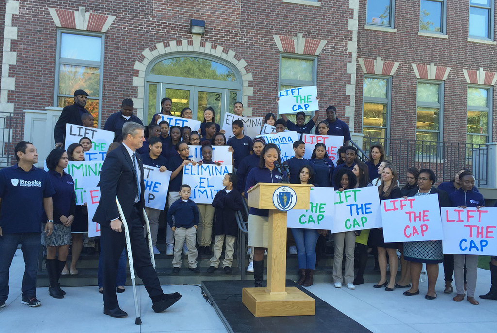 Gov. Charlie Baker flanked by several schoolchildren holding signs walks to announce proposed legislation on charter school caps