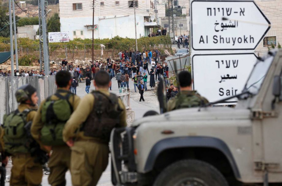 Israeli soldiers and Palestinians stand at the scene of a stabbing attack in the West Bank settlement of Kiryat Arba Monday Oct. 26 2015. The Israeli military said a Palestinian stabbed an Israeli in the West Bank before being shot and killed. Accordi