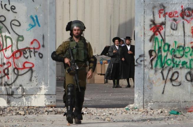 Orthodox Jewish men stand behind Israel's controversial separation barrier as a soldier makes his way through the West Bank entrance to Bethlehem