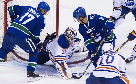 Anders Nilsson makes a save against Vancouver Canucks Brandon Sutter as Radim Vrbata looks for a rebound during the first period of an NHL hockey game Sunday Oct. 18 2015 in Vancouver British Columbia