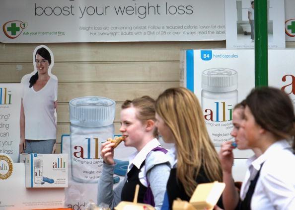 Schoolgirls eat fast food as they walk past a chemist stocking the Alli slimming pill