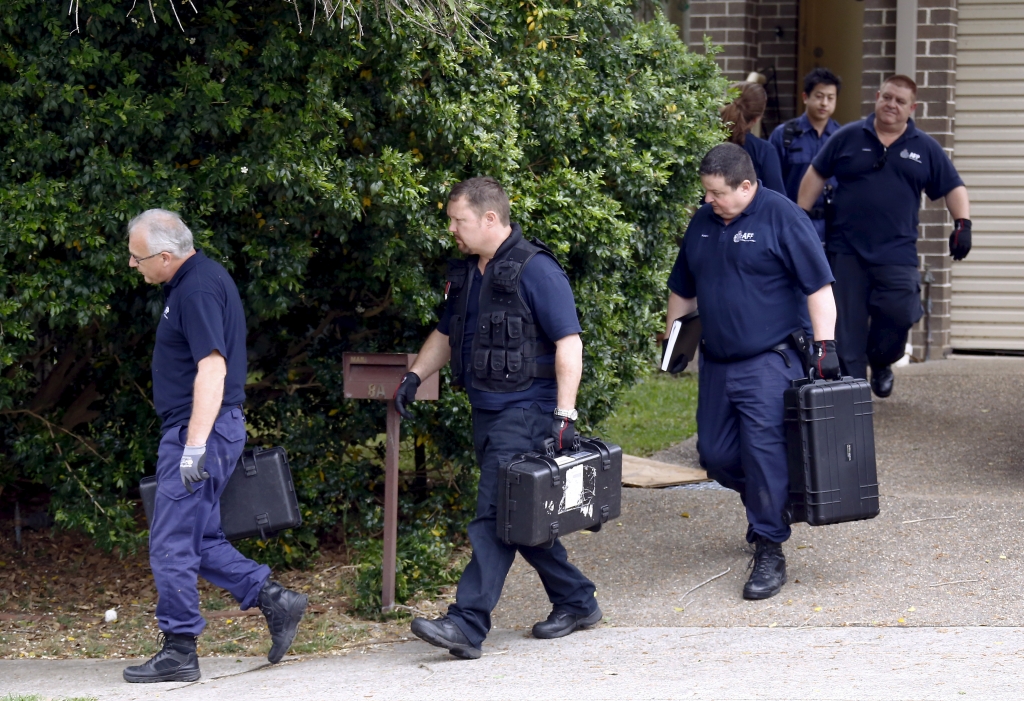 Australian Federal police officers carry equipment as they exit a house after arresting a man during early morning raids in western Sydney Australia