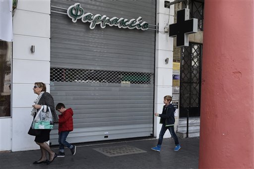 People walk past a shuttered pharmacy during the first day of a strike by the pharmacy owners association in the northern Greek city of Thessaloniki Monday Oct. 26 2015. Pharmacists are on strike to protest against new reforms in their sector. A leadin