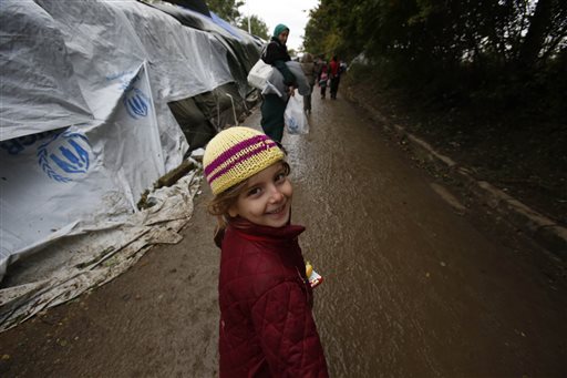 A migrant child smiles as she follows her mother down the path that leads to the Serbian Croatian border crossing at the village of Berkasovo near Sid Serbia on Thursday Oct.15 2015. The migrants and refugees are struggling with the autumn rain and