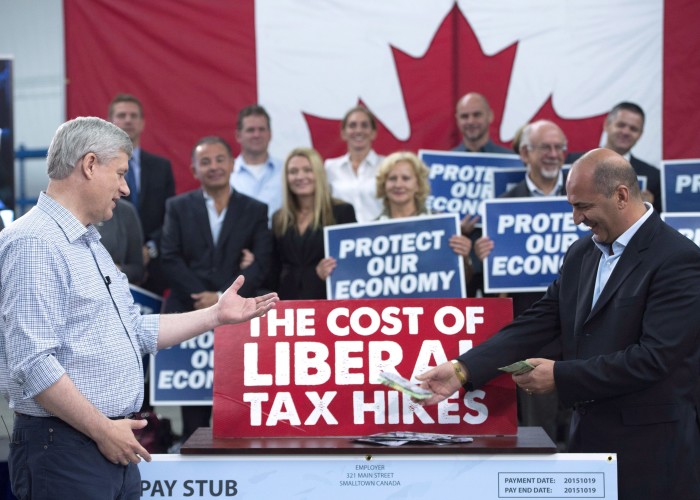 Conservative Leader Stephen Harper reacts as Dino Ari lays a pile of cash on the counter to illustrate the cost of proposed Liberal tax hikes during a campaign event at William F. White International in Etobicoke Ont. Tuesday Oct. 13 2015. THE CANADIA