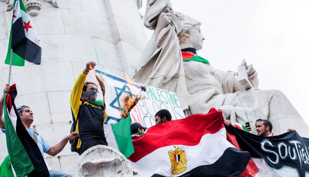 A pro Palestinian protester displays a burning Israeli flag during a demonstration at the Place de la Republique in Paris France Saturday