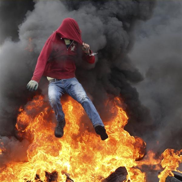 A Palestinian protester jumps over burning tyres during clashes with Israeli troops near the Jewish settlement of Bet El near the West Bank city of Ramallah on Monday. Prime Minister Benjamin Netanyahu has raised the possibility of revoking benefits and