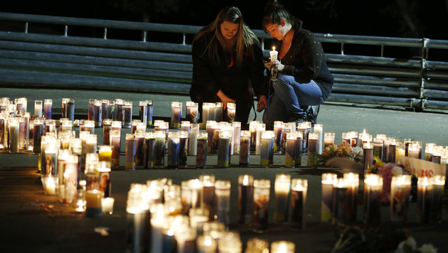 Two women pray by candles spelling out the initials of the community college that suffered a mass shooting on Oct. 1 2015