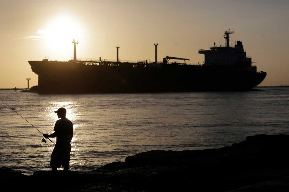 An oil tanker passes a fisherman as it enters a channel near Port Aransas heading for the Port of Corpus Christi. Defying a White House veto threat the Republican-controlled House has approved a bill to lift a 40-year-old U.S. ban on crude oil exports