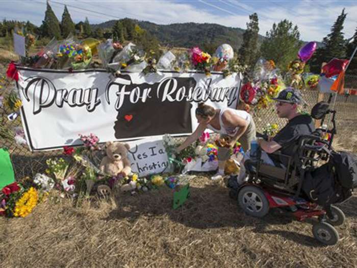 Candida Miller left and Brandon Snyder leave flowers at a site of a growing memorial to victims of the mass shooting at Umpqua Community College in Roseburg Ore. Tuesday Oct. 6 2015. AP