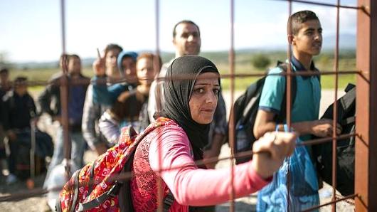 A woman stands behind a gate as she waits with other migrants and refugees to enter a registration camp after crossing the Greek Macedonia border