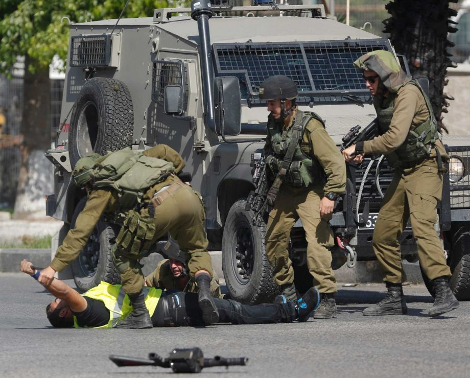 An Israeli soldier grabs a Palestinian's hand holding a knife after he stabbed another Israeli soldier seen on the ground during clashes in Hebron West Bank Friday Oct. 16 2015. The Palestinian man wearing a yellow'press vest and a T-shirt identify