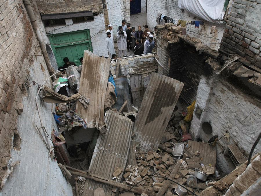 People stand outside a house damaged from an earthquake in Peshawar Pakistan