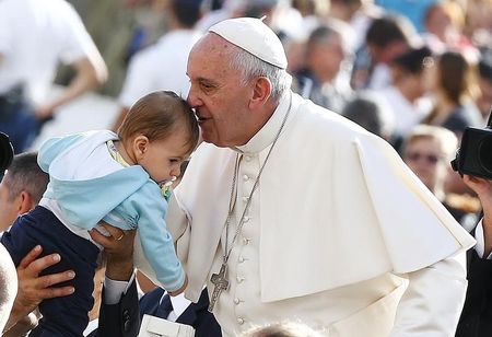 Pope Francis kisses a baby as he arrives to lead the weekly audience in Saint Peter's Square at the Vatican