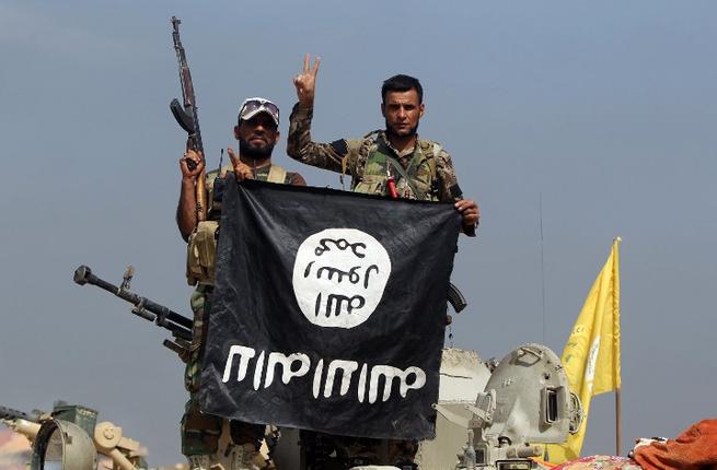 Popular Mobilisation unit fighters hold a Daesh flag upside down during a military operation in Baiji