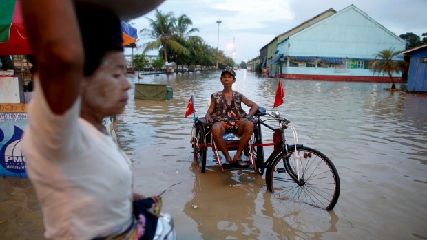 A man sits on his cart which he attached with National League for Democracy party flags along a flooded street in Yangon