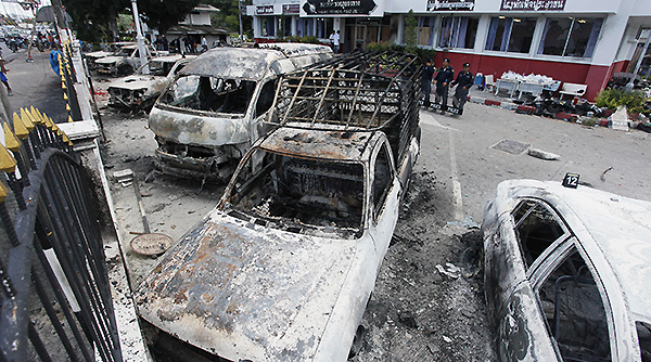 Thai policemen stand guard behind the burnt down vehicles at a police station in Phuket Thailand Sunday. Pic AP