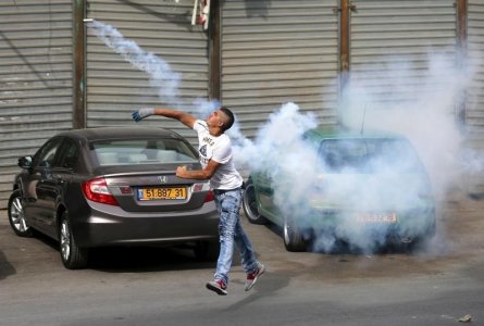 A Palestinian protester hurls back a tear gas canister fired by Israeli troops during clashes in the West Bank town of Al-Ram near Jerusalem