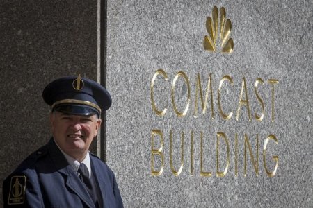 A Rockefeller Center guard stands next to the NBC logo and Comcast displayed on the building formerly known as the GE building in midtown Manhattan in New York