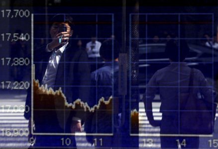 A man using a smartphone is reflected on a graph showing today's movements of Nikkei share average outside a brokerage in Tokyo Japan