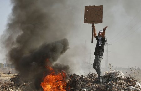 A Palestinian protester holding a sign shouts during clashes with Israeli troops near the border with Israel in the east of Gaza City in this