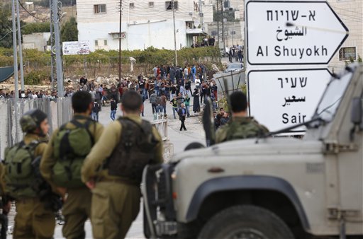 Israeli soldiers and Palestinians stand at the scene of a stabbing attack in the West Bank settlement of Kiryat Arba Monday Oct. 26 2015. The Israeli military said a Palestinian stabbed an Israeli in the West Bank before being shot and killed. Accordi