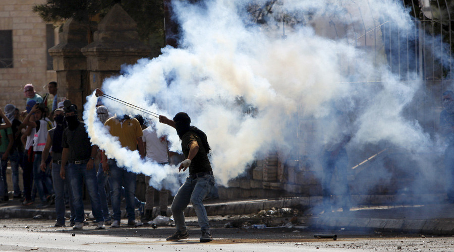 A Palestinian uses a sling to throw back a tear gas canister fired by Israeli troops during clashes in the West Bank city of Bethlehem