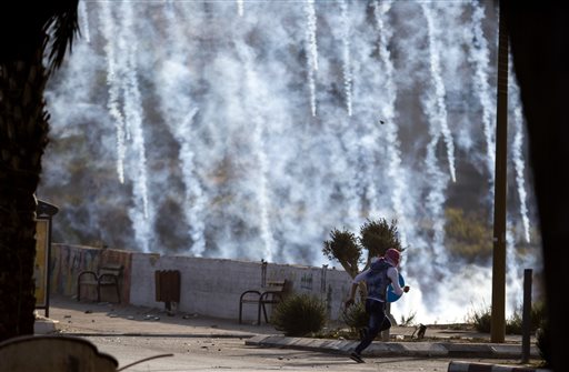 A Palestinian protester runs for cover from tear gas fired by Israeli soldiers during clashes with Israeli troops near Ramallah West Bank Saturday Oct. 17 2015. Israelis shot dead three Palestinians they said had attacked them with knives on Saturday