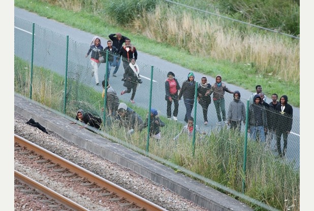 Migrants climb under a fence on to the tracks near the Eurotunnel site at Coquelles in Calais