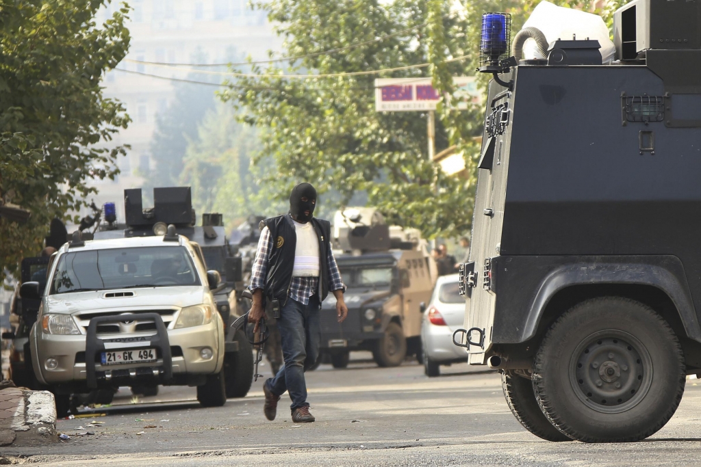 A masked police officer walks as armoured police vehicles block a road leading to the site of armed clashes with militants in Diyarbakir southeastern Turkey