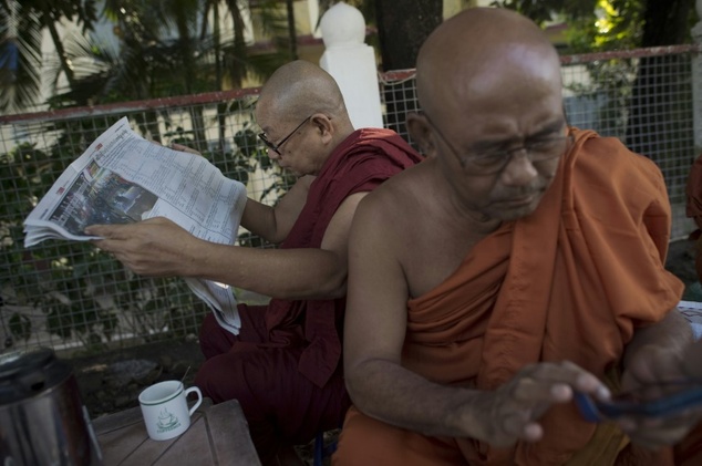 A Buddhist monk reads a newspaper as another browses his smartphone in Yangon