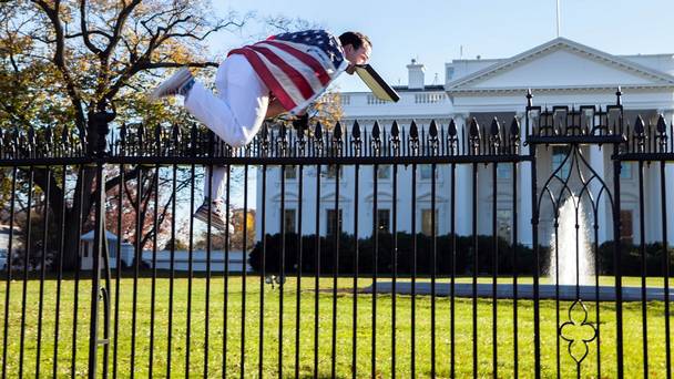 A man with a US flag wrapped around him jumps the fence at the White House