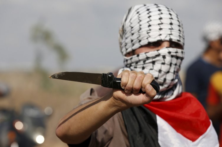 A masked Palestinian protester holds a knife during a protest near the Israeli border fence in northeast Gaza