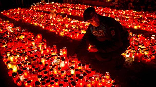 A police officer places a candle collected from people waiting to pay respects to the victims of a fire in Bucharest