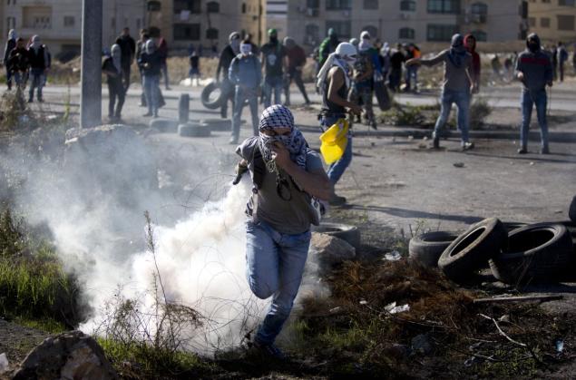 A Palestinian throws back a tear gas canister that was fired by Israeli troops during clashes in the West Bank city of Ramallah on Friday