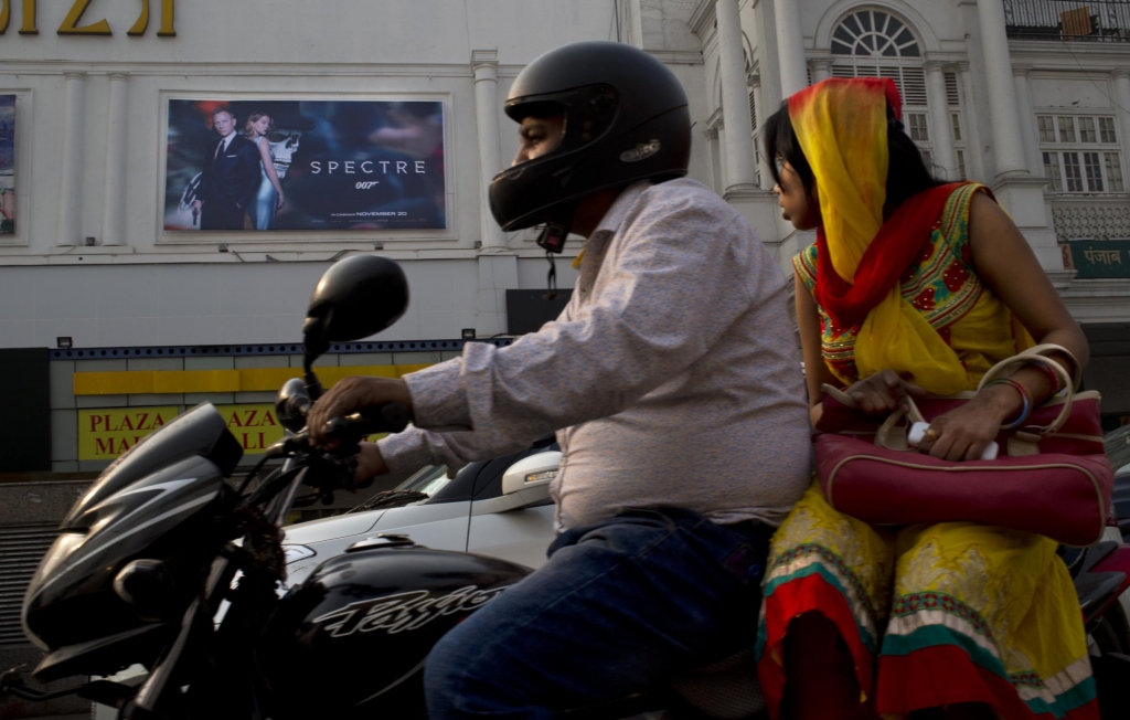 An Indian couple rides past a movie hall displaying a poster of the latest James Bond movie