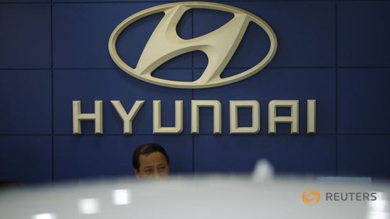 An employee sits in front of the logo of Hyundai Motor Co. at its dealership in Seoul South Korea