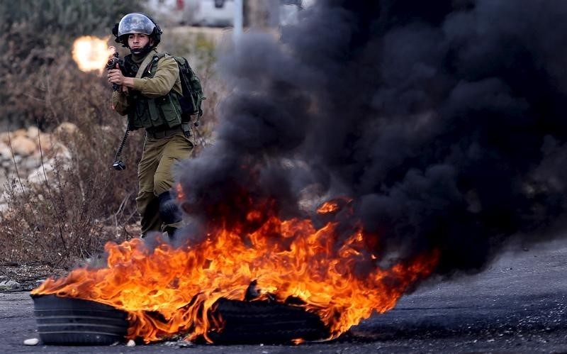 An Israeli soldier fires a weapon towards Palestinian protesters during clashes near the Jewish settlement of Bet El near the West Bank city of Ramallah